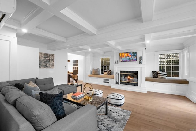 living room featuring crown molding, beam ceiling, light wood-style flooring, a glass covered fireplace, and coffered ceiling