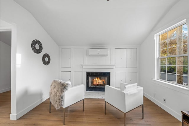 living area with vaulted ceiling, a fireplace with flush hearth, plenty of natural light, and a wall mounted air conditioner