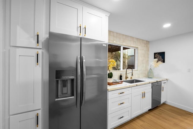 kitchen with backsplash, light wood-type flooring, appliances with stainless steel finishes, white cabinets, and a sink