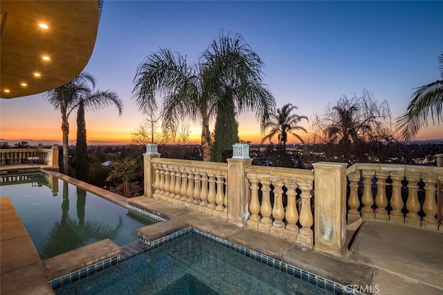 pool at dusk featuring a pool with connected hot tub