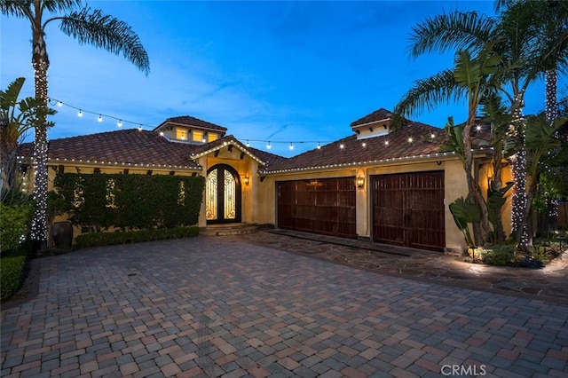 mediterranean / spanish-style home featuring stucco siding, an attached garage, a tile roof, and decorative driveway