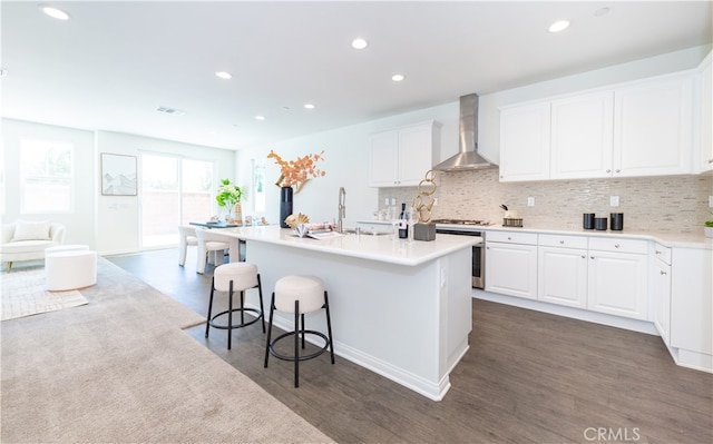 kitchen featuring white cabinetry, wall chimney range hood, a breakfast bar area, and tasteful backsplash