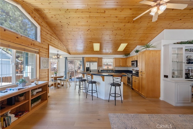 kitchen featuring a kitchen bar, dark countertops, stainless steel appliances, wooden ceiling, and light wood finished floors