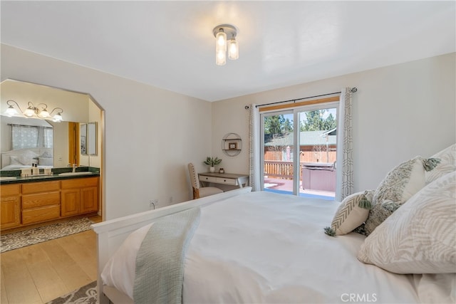 bedroom with access to exterior, light wood finished floors, ensuite bathroom, and a sink