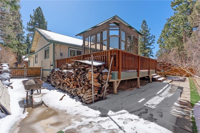 snow covered back of property featuring a deck and fence