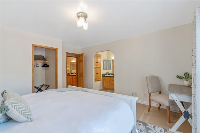 bedroom featuring baseboards, ensuite bath, and light wood-style flooring