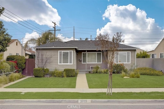 bungalow with a front lawn, fence, and roof with shingles