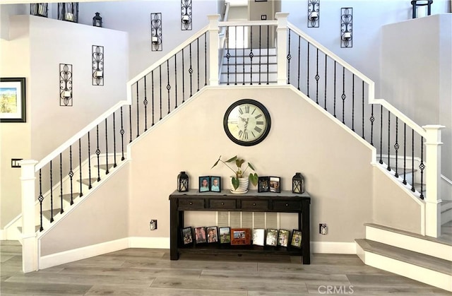 stairway featuring a high ceiling, baseboards, and wood finished floors