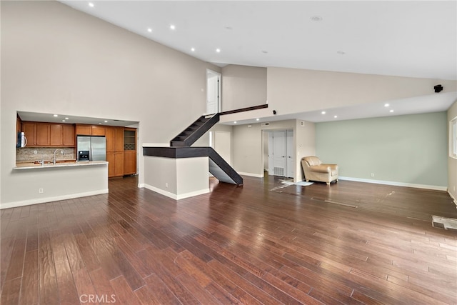 unfurnished living room with stairway, dark wood-style floors, baseboards, and a sink