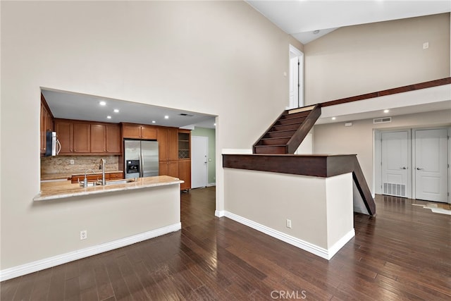 kitchen featuring appliances with stainless steel finishes, a peninsula, brown cabinetry, high vaulted ceiling, and a sink