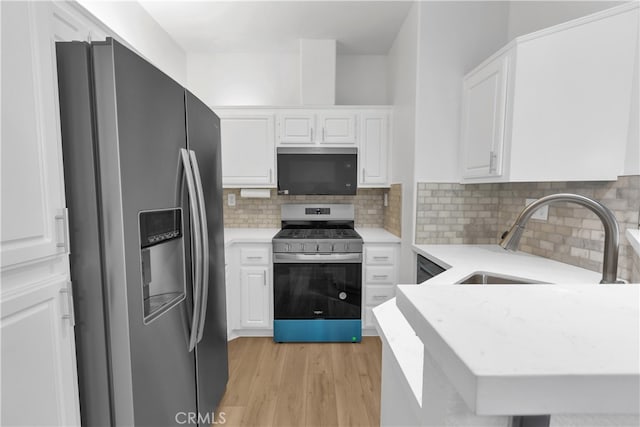 kitchen with light wood finished floors, decorative backsplash, white cabinets, stainless steel appliances, and a sink