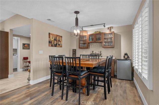 dining room featuring wood finished floors, visible vents, baseboards, an inviting chandelier, and rail lighting