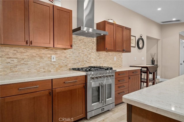 kitchen featuring brown cabinetry, decorative backsplash, high end stainless steel range oven, and wall chimney range hood