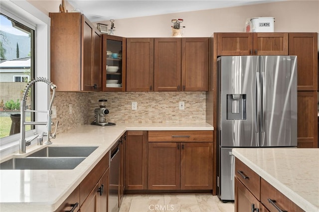 kitchen with a sink, stainless steel appliances, glass insert cabinets, and tasteful backsplash