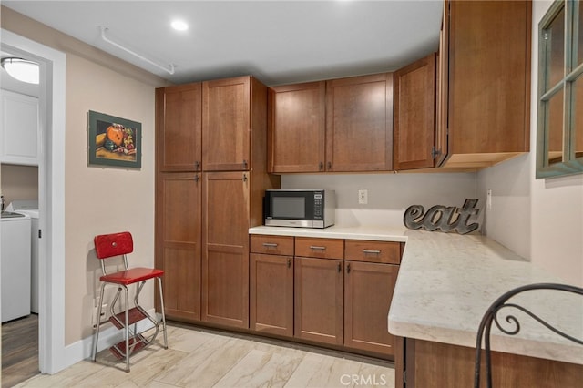 kitchen with brown cabinetry, stainless steel microwave, washer and dryer, and light countertops