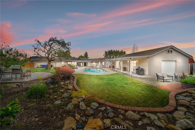 back of property at dusk with stucco siding, fence, a yard, an outdoor pool, and a patio area