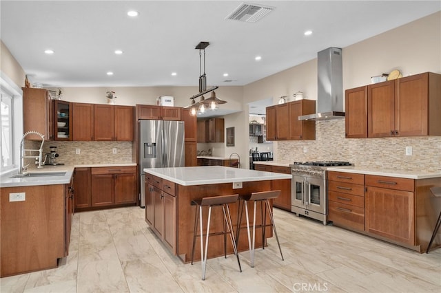 kitchen featuring visible vents, a center island, wall chimney range hood, stainless steel appliances, and a sink