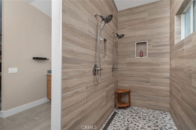 bathroom featuring tiled shower, vanity, and baseboards