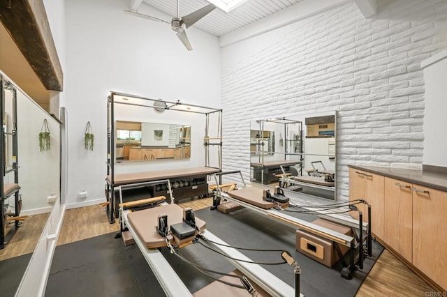 workout room with brick wall, ceiling fan, baseboards, a towering ceiling, and dark wood-style floors