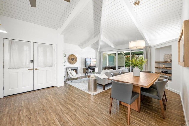 dining space with a fireplace, vaulted ceiling with beams, wood finished floors, and baseboards