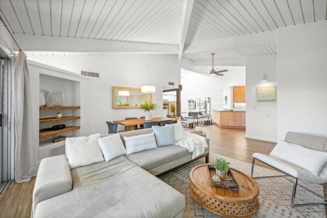 living area featuring ceiling fan, lofted ceiling with beams, visible vents, and light wood-type flooring