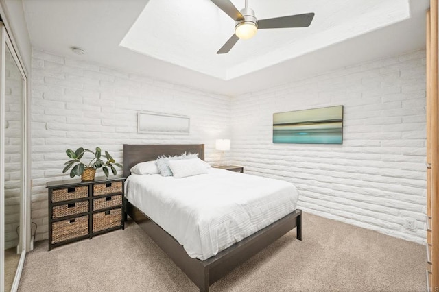 carpeted bedroom with brick wall, a raised ceiling, and ceiling fan