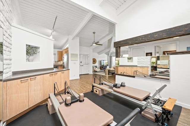 workout room featuring baseboards, ceiling fan, rail lighting, wood finished floors, and high vaulted ceiling