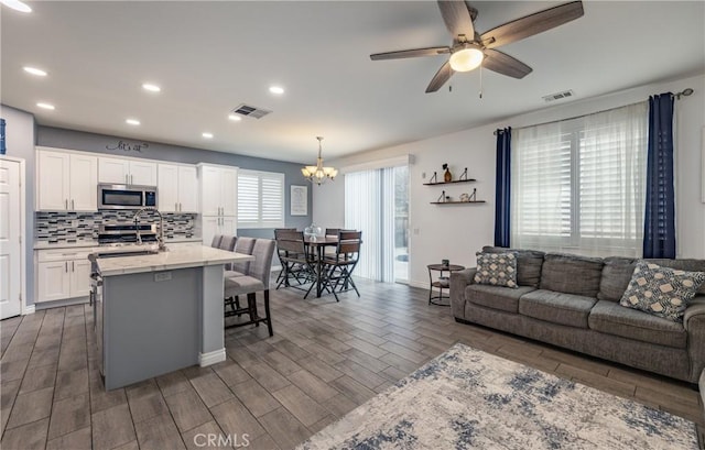 living room featuring recessed lighting, visible vents, ceiling fan with notable chandelier, and dark wood-type flooring