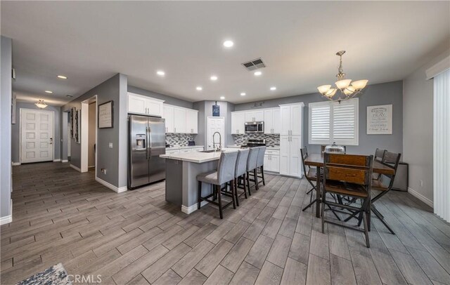 kitchen with visible vents, decorative backsplash, appliances with stainless steel finishes, white cabinetry, and a kitchen breakfast bar