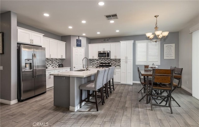 kitchen featuring visible vents, wood finish floors, stainless steel appliances, white cabinetry, and a sink