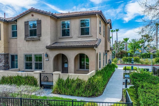 mediterranean / spanish-style house featuring stucco siding, a fenced front yard, and a tiled roof