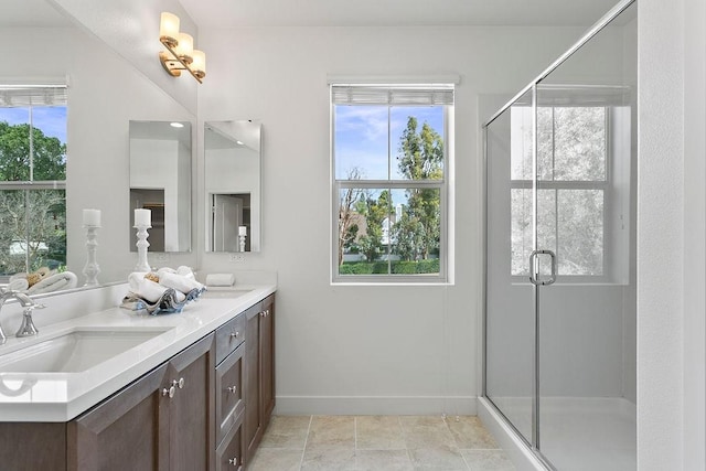 full bath featuring baseboards, double vanity, a stall shower, tile patterned floors, and a sink