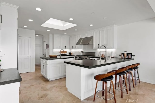 kitchen with gas stove, a skylight, a sink, under cabinet range hood, and dark countertops