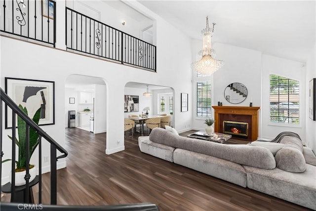 living area featuring dark wood-style floors, a high ceiling, arched walkways, a lit fireplace, and a chandelier