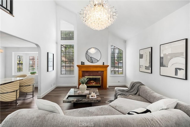 living area featuring a fireplace with flush hearth, wood finished floors, a high ceiling, baseboards, and a chandelier