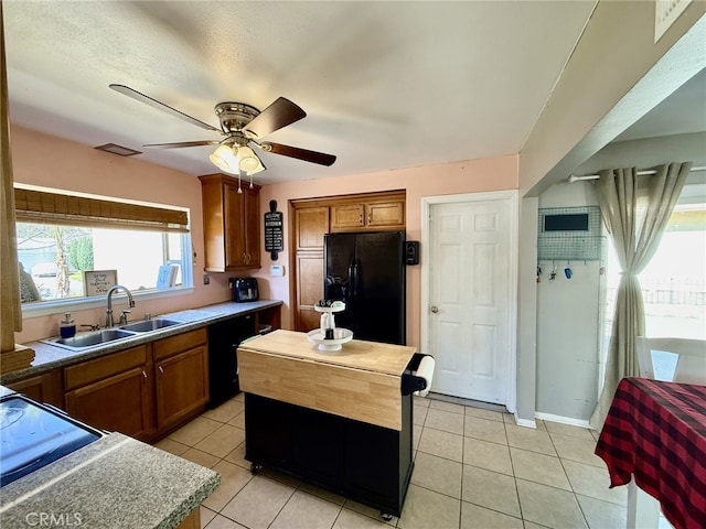 kitchen with black appliances, light tile patterned flooring, brown cabinetry, and a sink