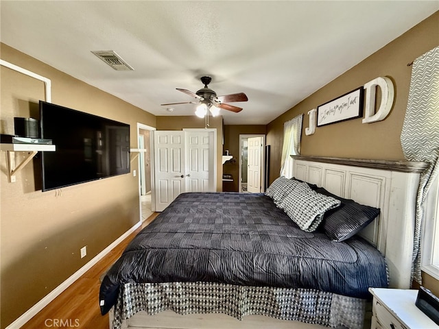 bedroom with a ceiling fan, wood finished floors, baseboards, visible vents, and ensuite bathroom