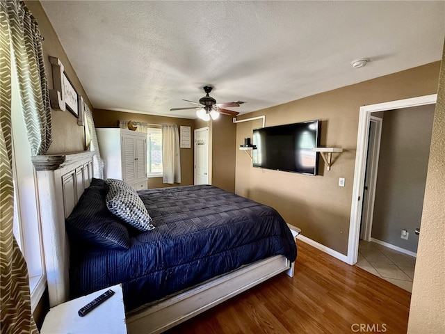 bedroom with baseboards, a textured ceiling, wood finished floors, and a ceiling fan