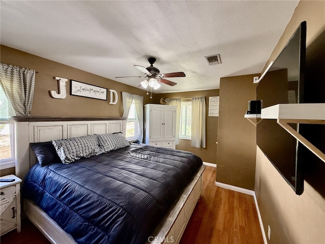 bedroom featuring wood finished floors, baseboards, visible vents, ceiling fan, and a textured ceiling