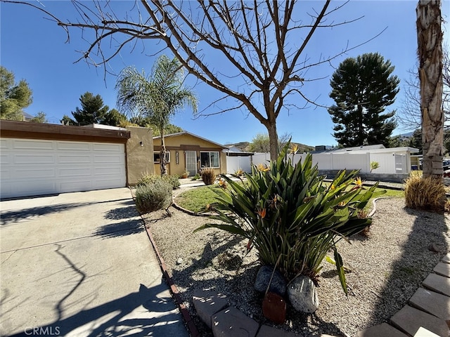 view of front of house featuring stucco siding, driveway, an attached garage, and fence