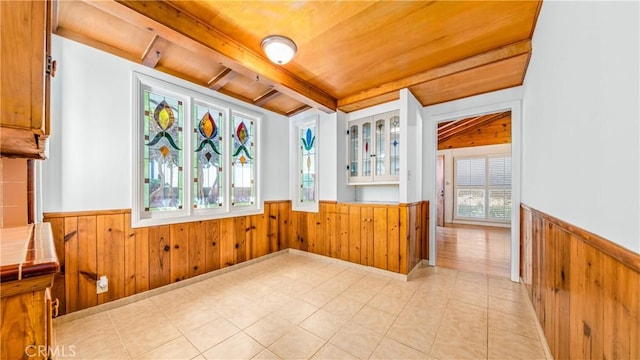 interior space featuring beam ceiling, wooden walls, tile counters, and wainscoting