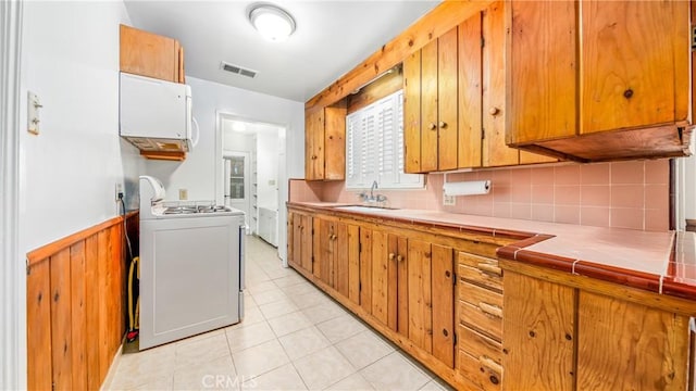 kitchen with visible vents, a sink, gas range oven, wainscoting, and tile counters