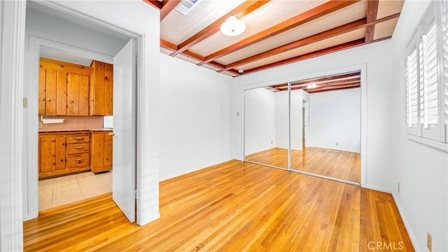 unfurnished bedroom featuring a closet, beam ceiling, light wood-style floors, and visible vents