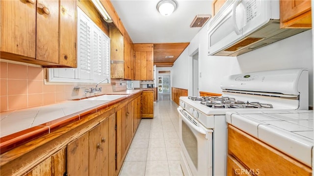 kitchen with white appliances, tile counters, brown cabinets, and a sink