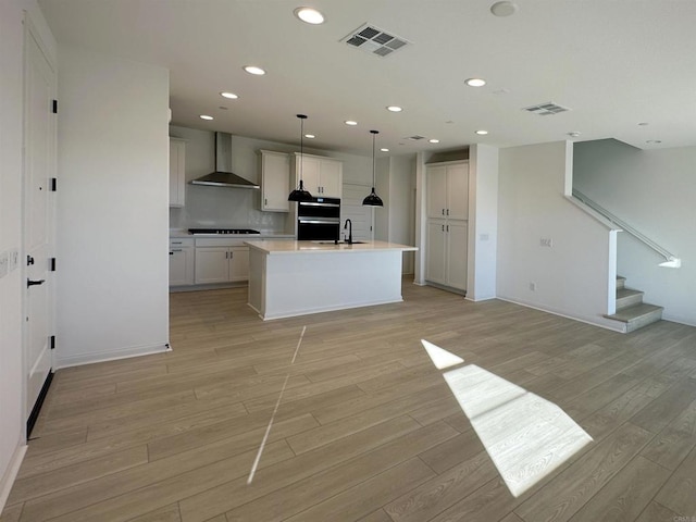 kitchen with light wood finished floors, visible vents, light countertops, stovetop, and wall chimney exhaust hood