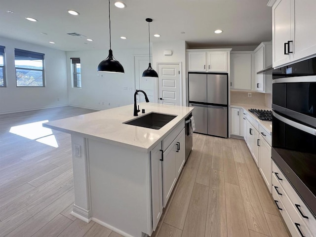 kitchen featuring light wood finished floors, recessed lighting, a sink, hanging light fixtures, and appliances with stainless steel finishes