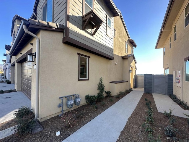 view of side of home with stucco siding, fence, and a gate