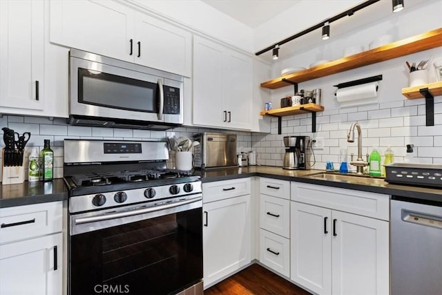 kitchen featuring dark countertops, tasteful backsplash, open shelves, stainless steel appliances, and a sink