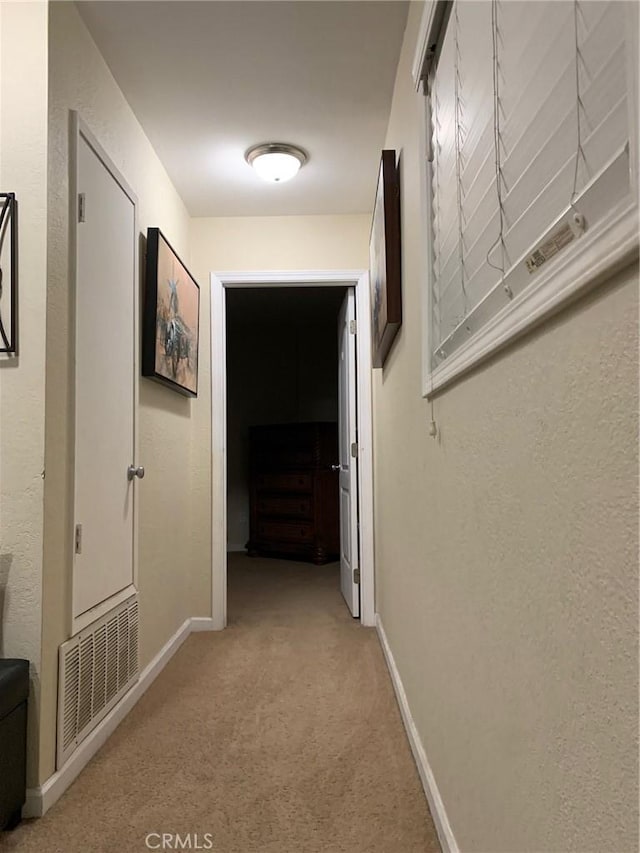 hallway featuring light colored carpet, visible vents, and baseboards