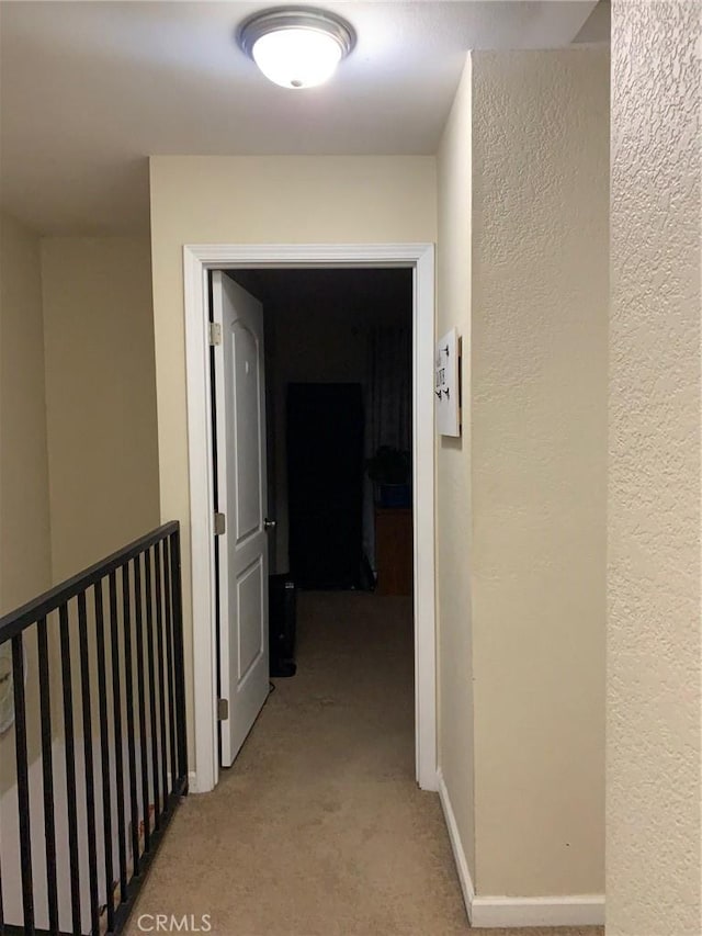 hallway with baseboards, light carpet, and a textured wall